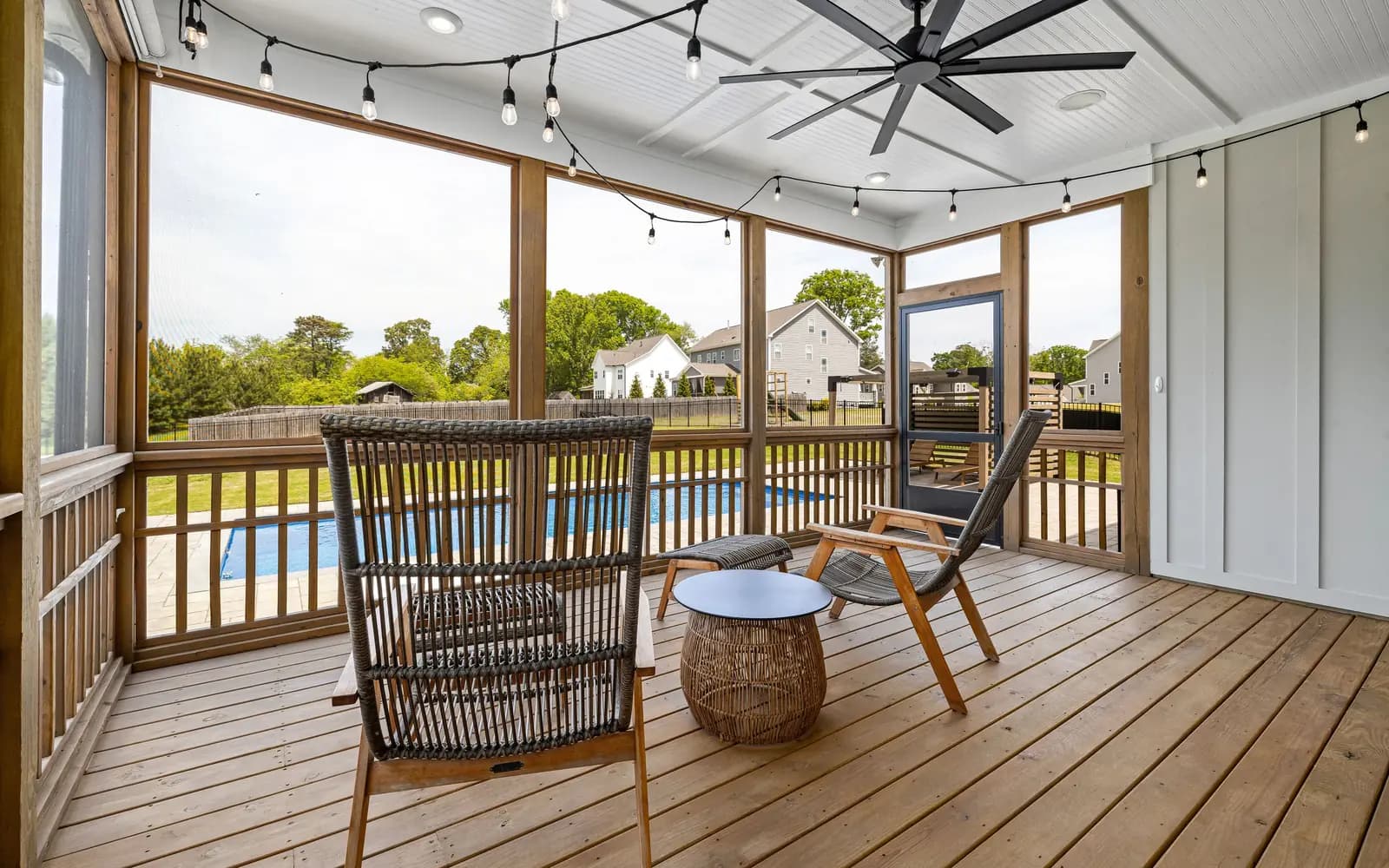 Galería exterior con ventilador de techo, sillones de mimbre y madera, mesa auxiliar y piscina al fondo