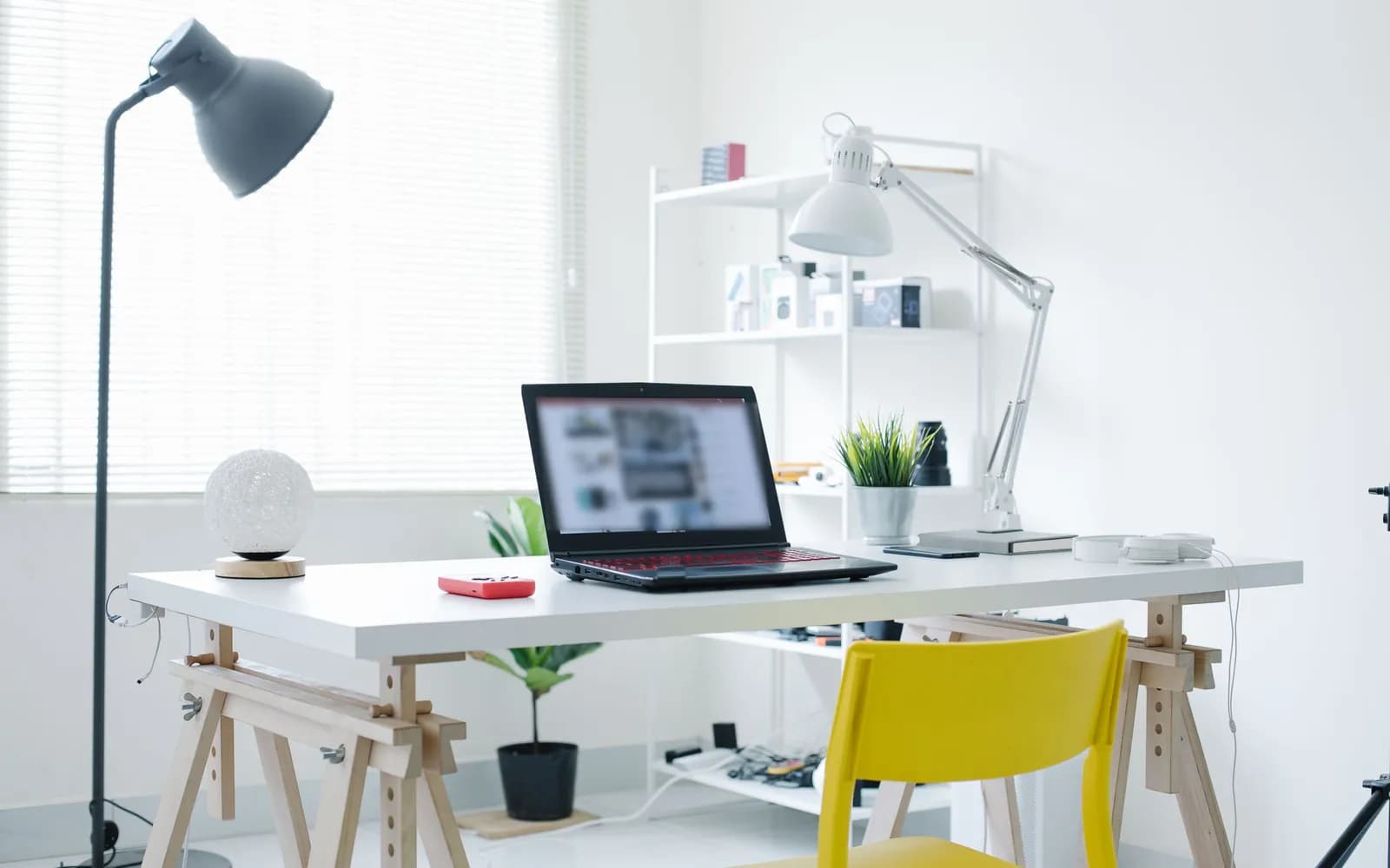 Oficina en casa luminosa con notebook sobre un escritorio blanco, silla amarilla, auriculares y estantería